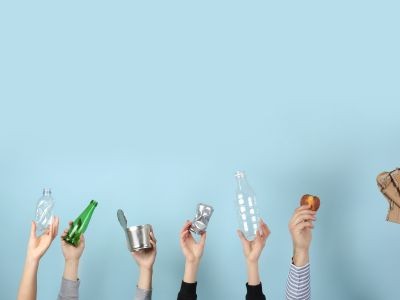 mains tenant une bouteille en verre, une bouteille en plastique, une boîte de conserve,  une demie tomate