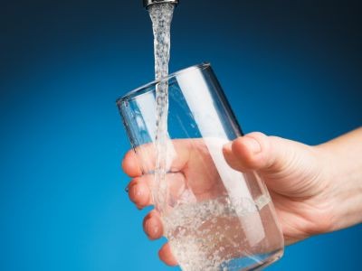 eau coulant d'un robinet dans un verre tenu par une main