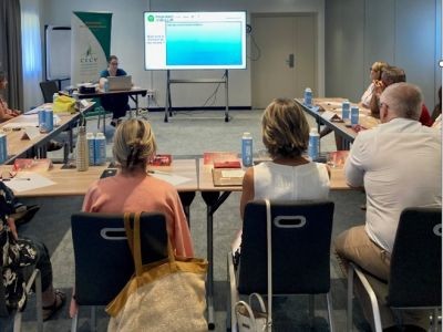 hommes et femmes de dos assis autour d'une table devant un écran