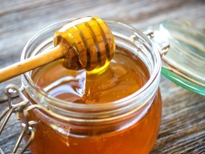 pot de miel en verre avec une spatule en bois dégoulinant de miel posée dessus