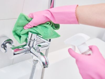 main avec un gant rose qui tient un chiffon vert sur un robinet