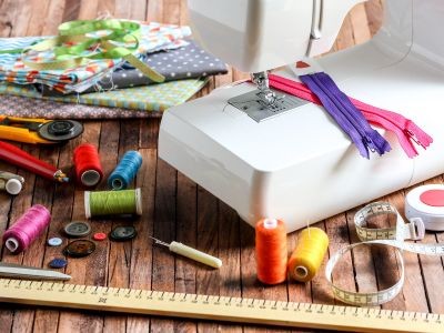 posés sur une table en bois : une machine à coudre, dés à coudre, fils, fermetures éclair, metre ruban, tissu aiguilles ciseaux, règle