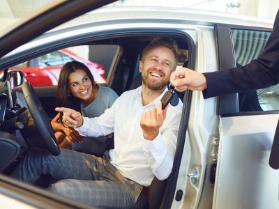 femme homme qui sourient assis dans une voiture porte avant conducteur ouverte l'homme tient une clé donnée pat une main